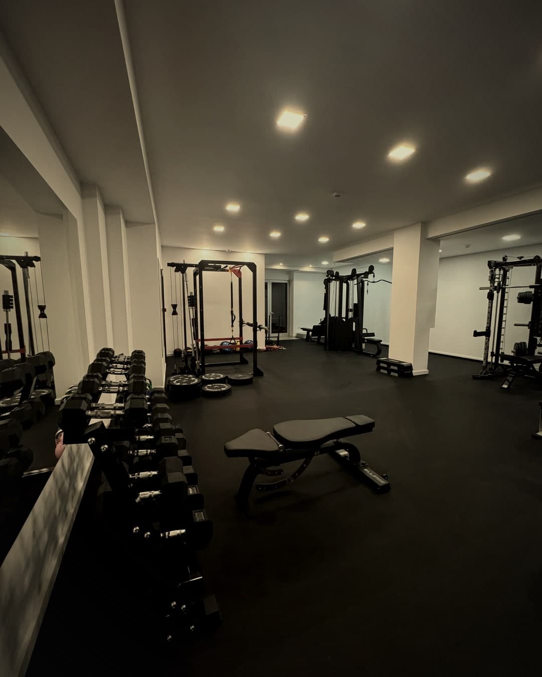 Sala de treino do RØØKY: rack, banco ajustável e halteres sobre chão preto